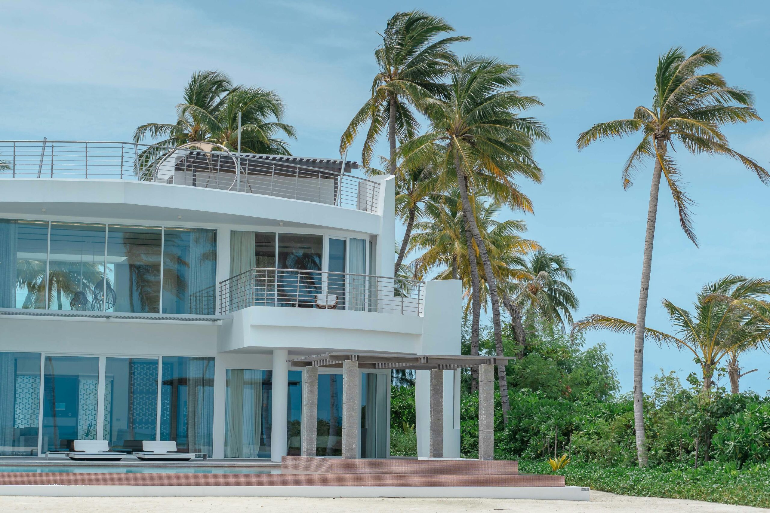 Nos biens Beautiful beachfront villa with palm trees and ocean view, ideal for vacation and relaxation.