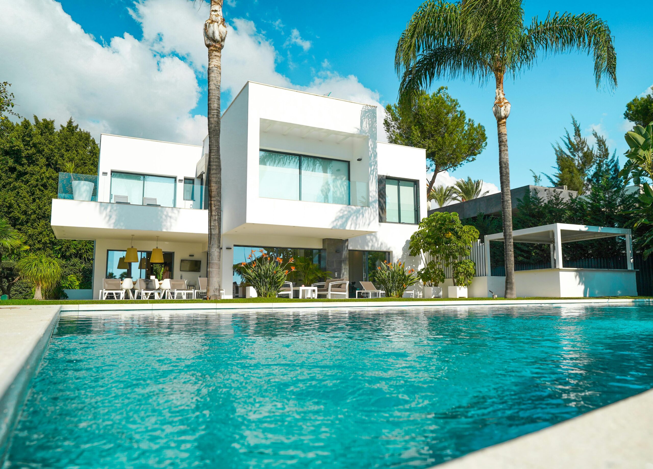Nos biens A stunning modern luxury villa with a pool, surrounded by lush greenery and bathed in sunlight.