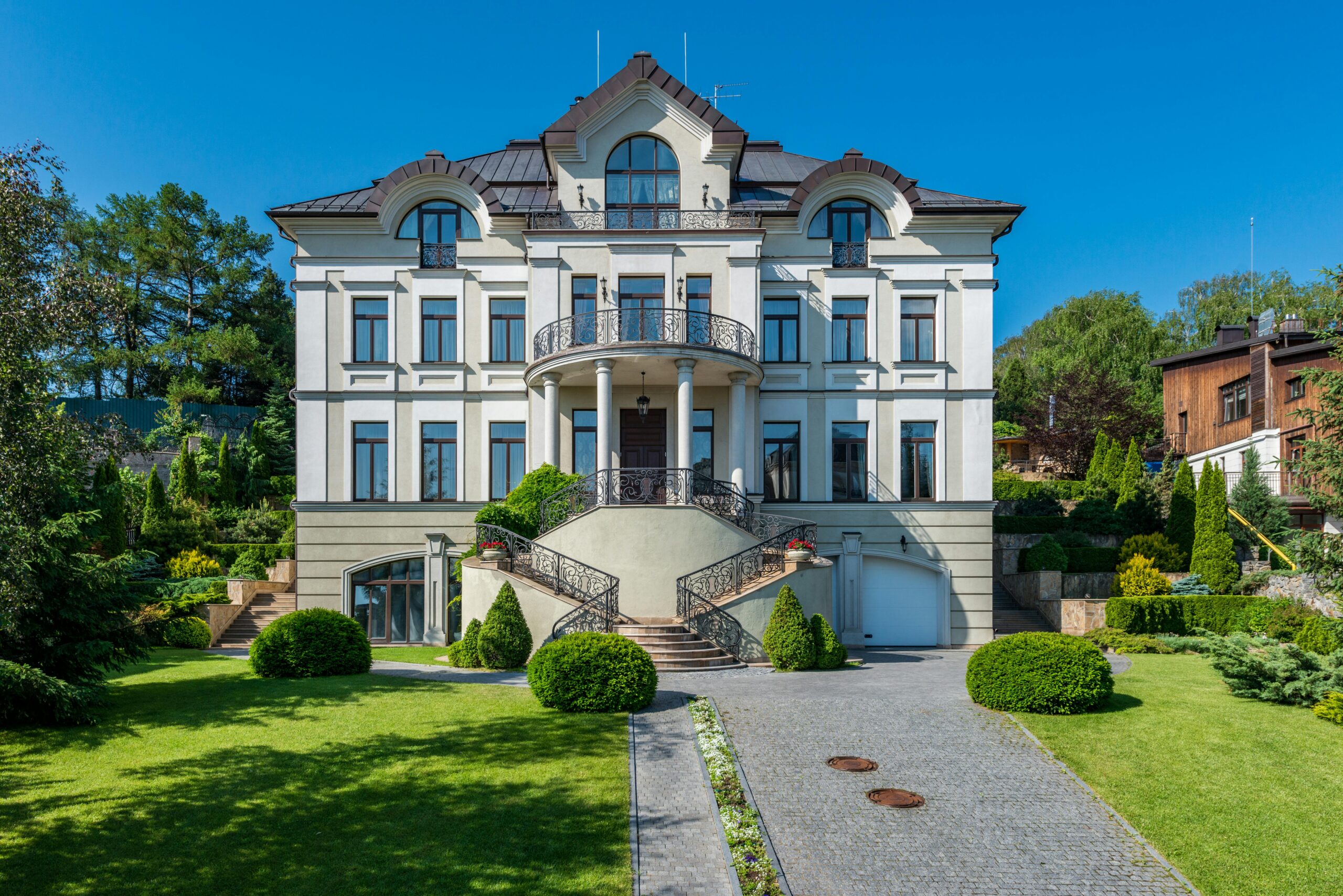 Nos biens Exterior of large residential building with steps and metal railing surrounded with fresh verdant grass and bushes with trees
