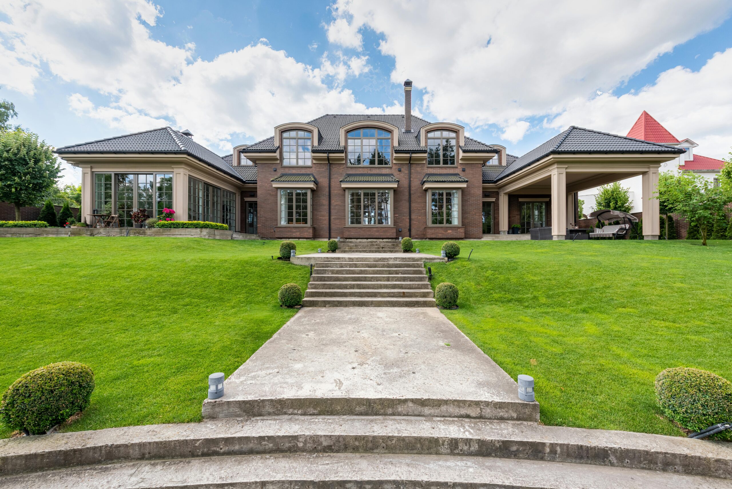 Nos biens Elegant upscale mansion with lush green garden and clear blue sky.